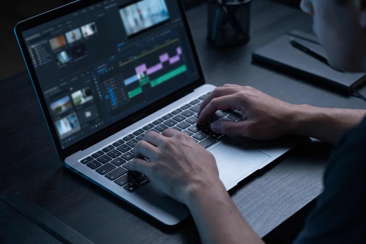 Hands editing video on an Apple MacBook Air at night