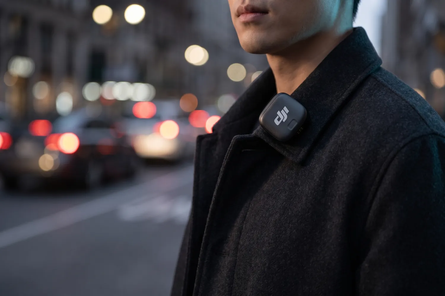 DJI Mic 3 transmitter clipped to a coat collar on a city street at dusk