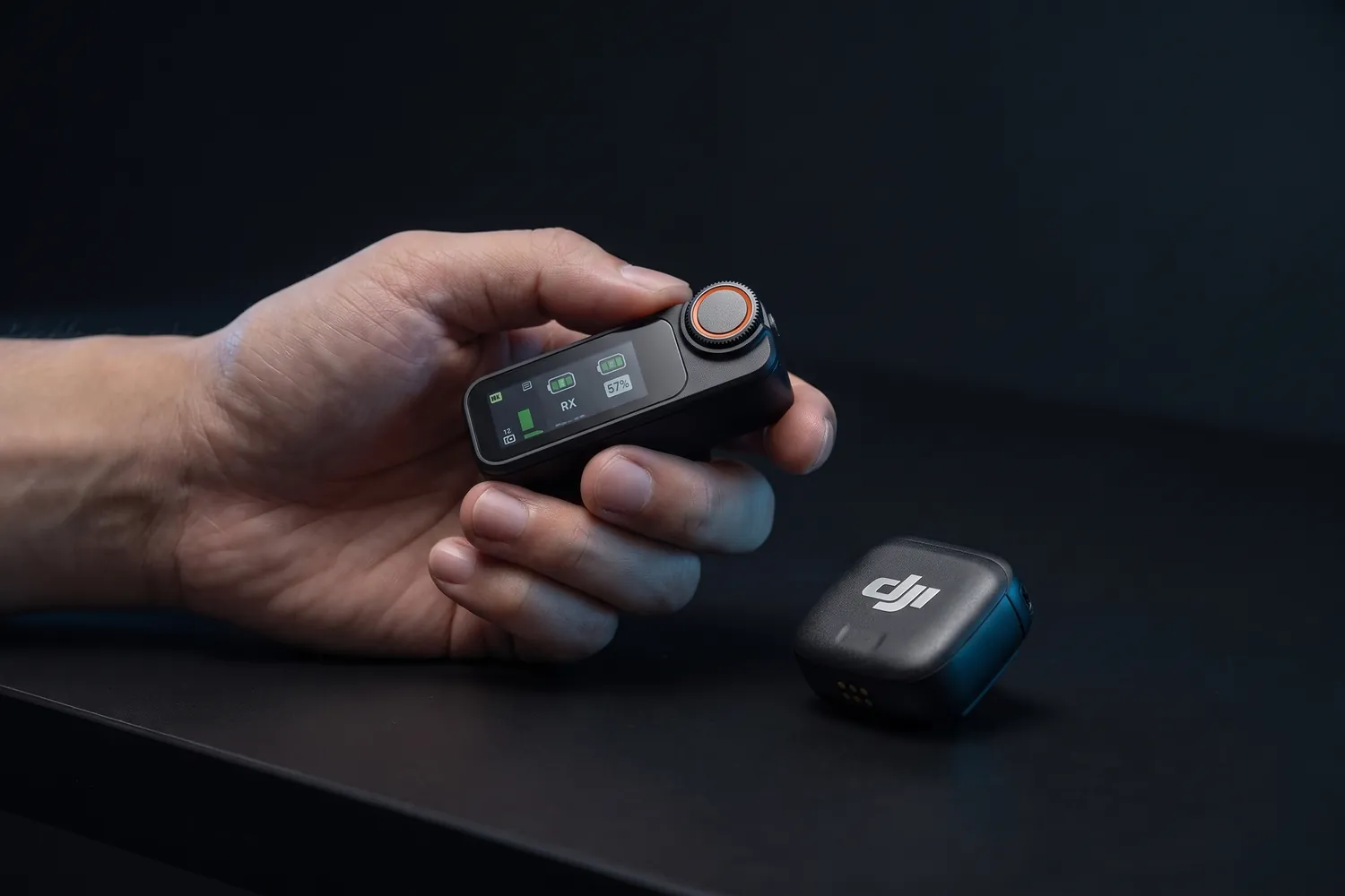 DJI Mic 3 receiver with its touchscreen and dial in a hand, a transmitter beside it